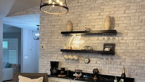 A modern living room with a fireplace, two leather armchairs, a round ottoman, and a coffee bar with shelves above. - Pelican’s Cove, Gulf Access, Pool, & Dock (Cape Coral)