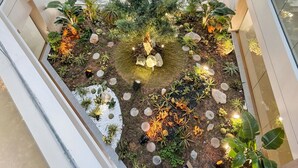 A multi-level atrium with a central garden area featuring a variety of plants, rocks, and a small water feature. - Stylish 1BR with PS5, Sauna and Kids` Play Area (Dubai)