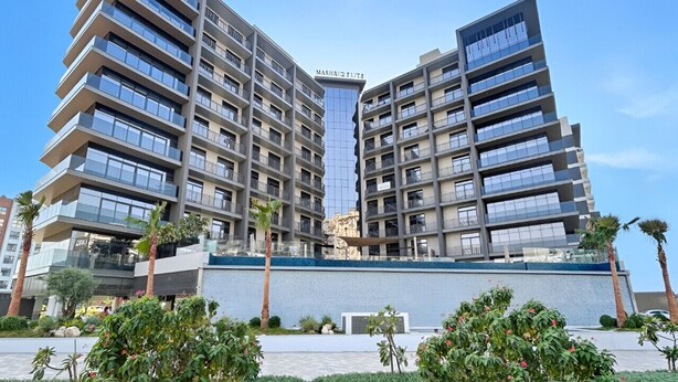 A modern high-rise building with multiple balconies and a central glass facade. - Stylish 1BR with PS5, Sauna and Kids` Play Area (Dubai)