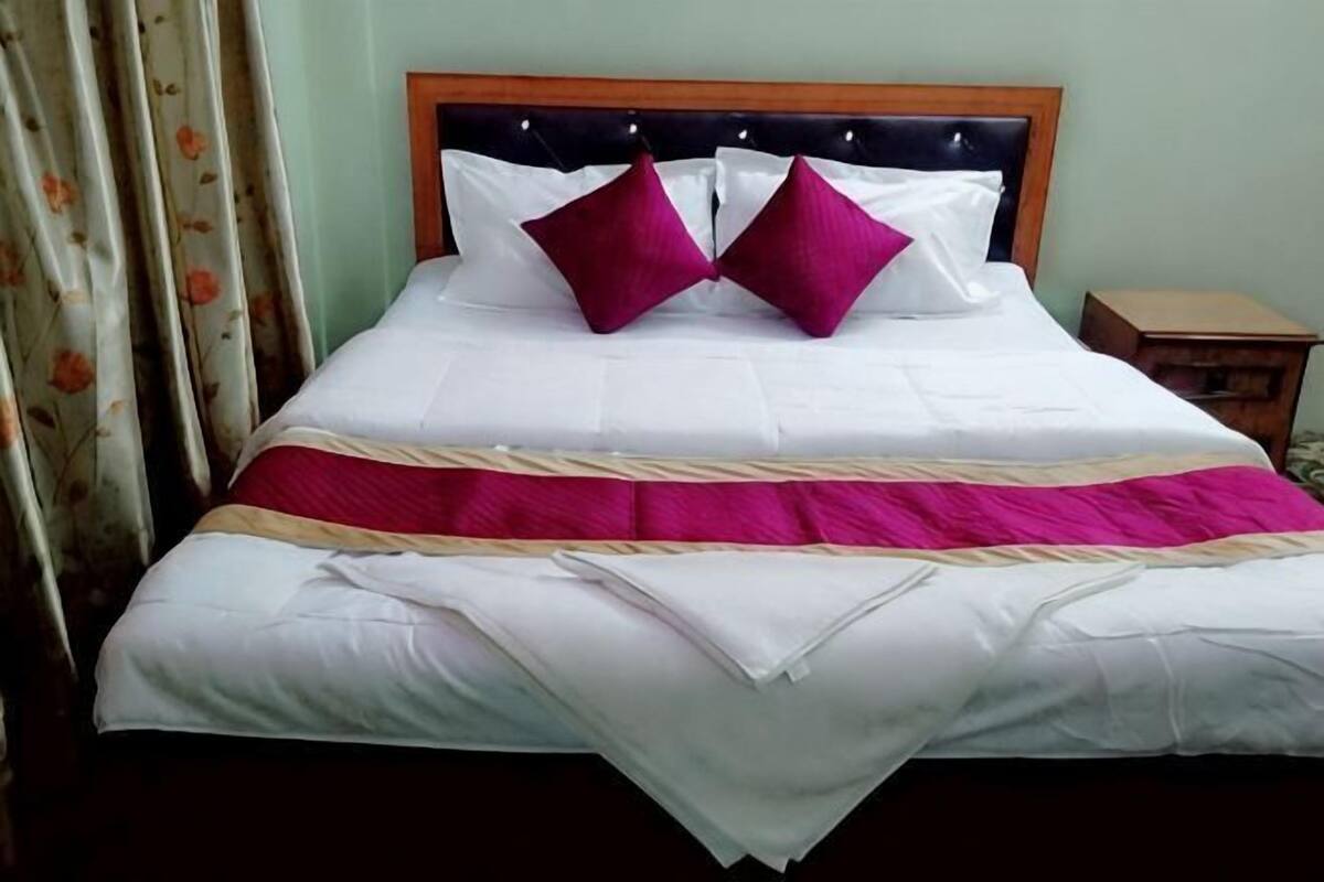 Una cama con cabecera de madera, ropa de cama blanca y dos almohadas rosas.