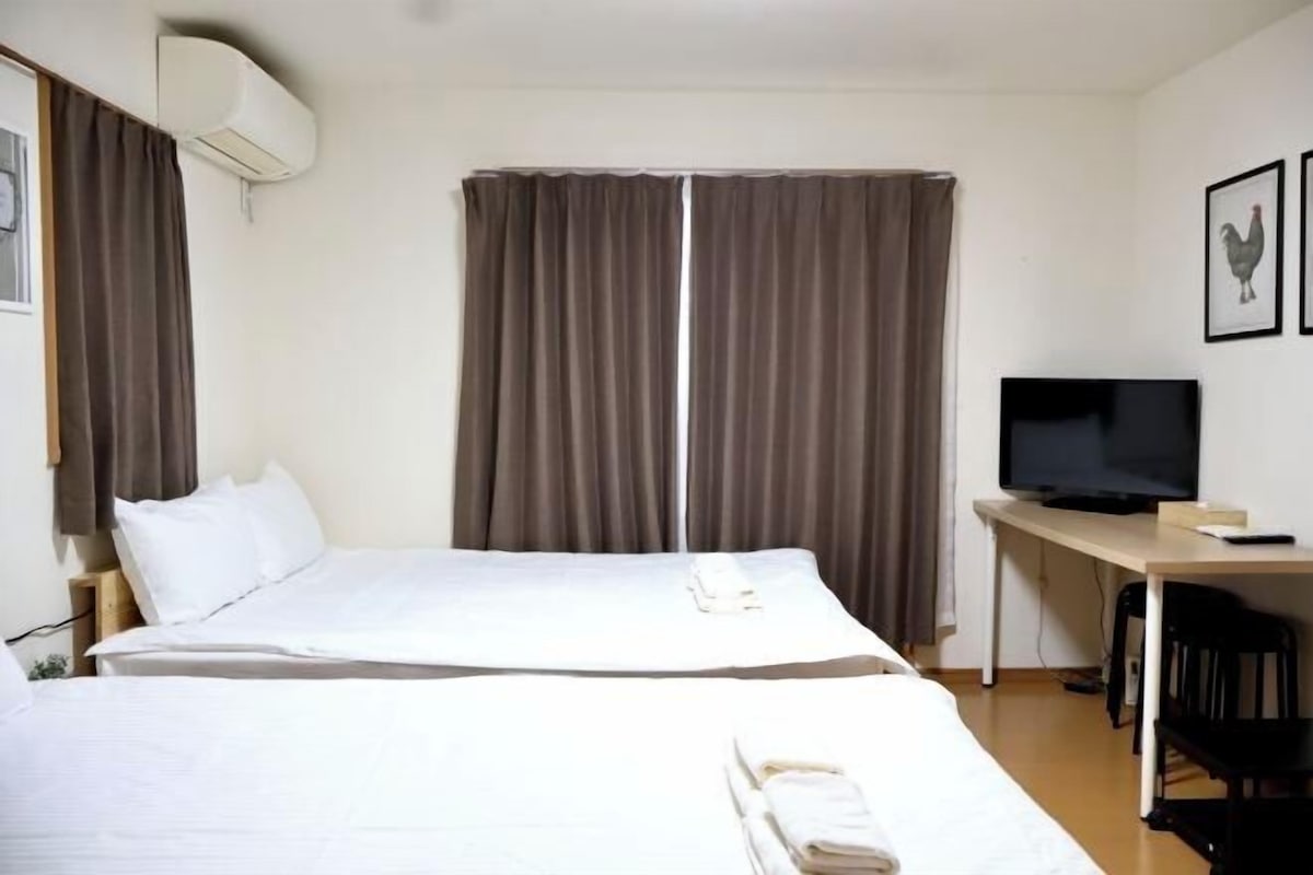 A hotel room with two beds, a desk with a television, and curtains.
