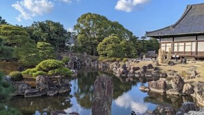 A traditional Japanese garden with a pond, rocks, and a building with a tiled roof.