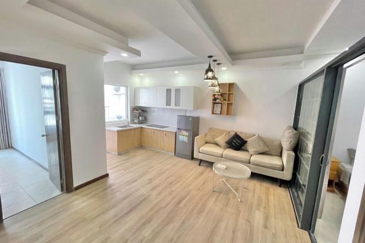 A modern apartment with a kitchenette, a sofa, and a glass door leading to a balcony.