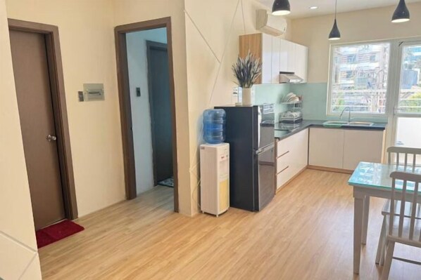 A compact kitchen with a refrigerator, a water dispenser, and a window with a city view. - Muong Thanh Hon Chong Apartment with Sea View (Nha Trang)