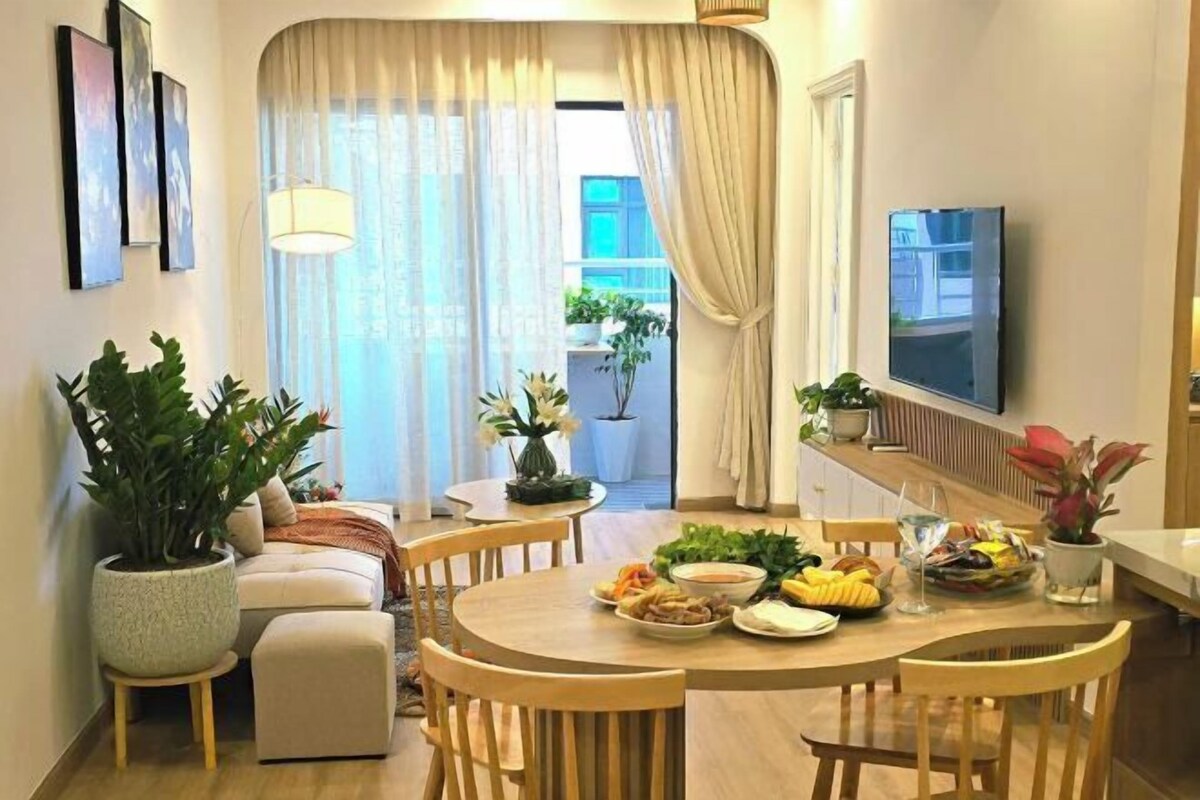 A dining area with a round table, chairs, potted plants, and a TV mounted on the wall.