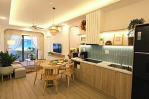 A modern kitchen with wooden cabinets, a dining area with a round table and chairs, and a view of the outdoors through a large window. - Muong Thanh Hon Chong Apartment with Sea View (Nha Trang)