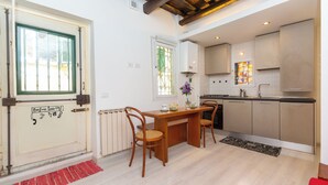 A compact kitchen with a dining area, featuring a wooden table, chairs, and a radiator. - Rental in Rome Campo De Fiori Apartment (Rome)