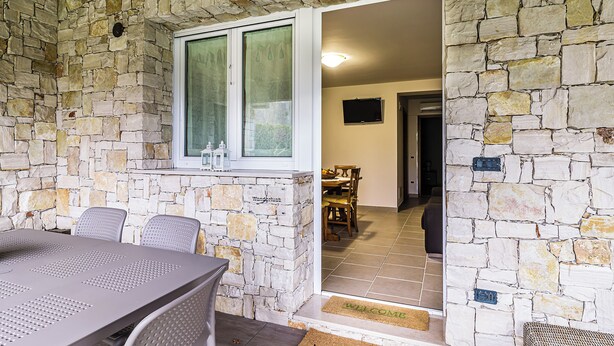 A stone-walled room with a dining table and chairs, a window, and a welcome mat. - Apt Wanderlust 1 with swimming pool[Unesco-Prosecco] (Bagnolo)