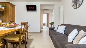 A modern living room with a dark grey sofa, a wooden dining table with chairs, and a flat-screen TV displaying "NETFLIX". - Apt Wanderlust 1 with swimming pool[Unesco-Prosecco] (Bagnolo)