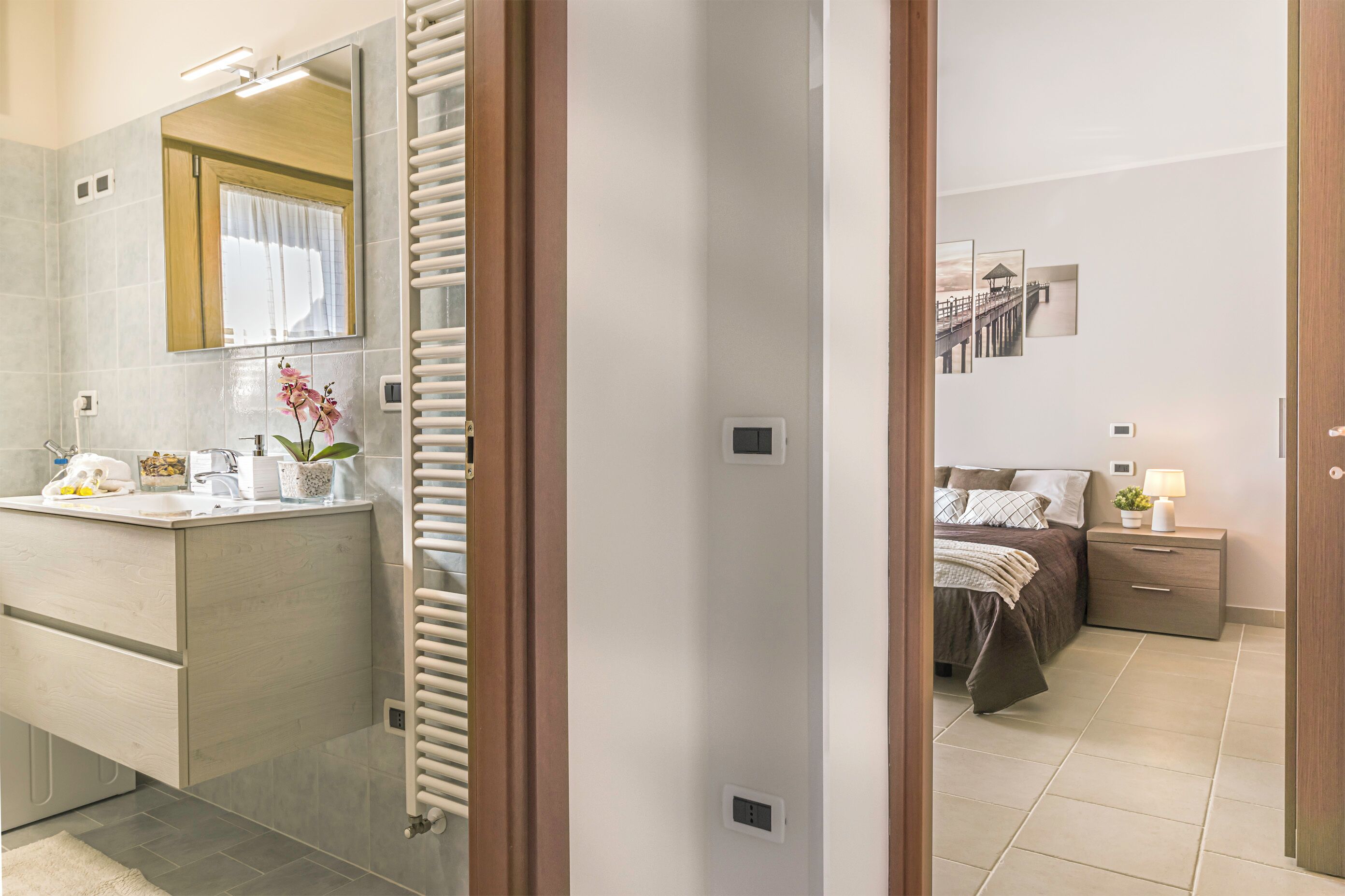 A modern bathroom with a large mirror, a toilet, and a sink. There is a towel rack and a potted plant on the counter.