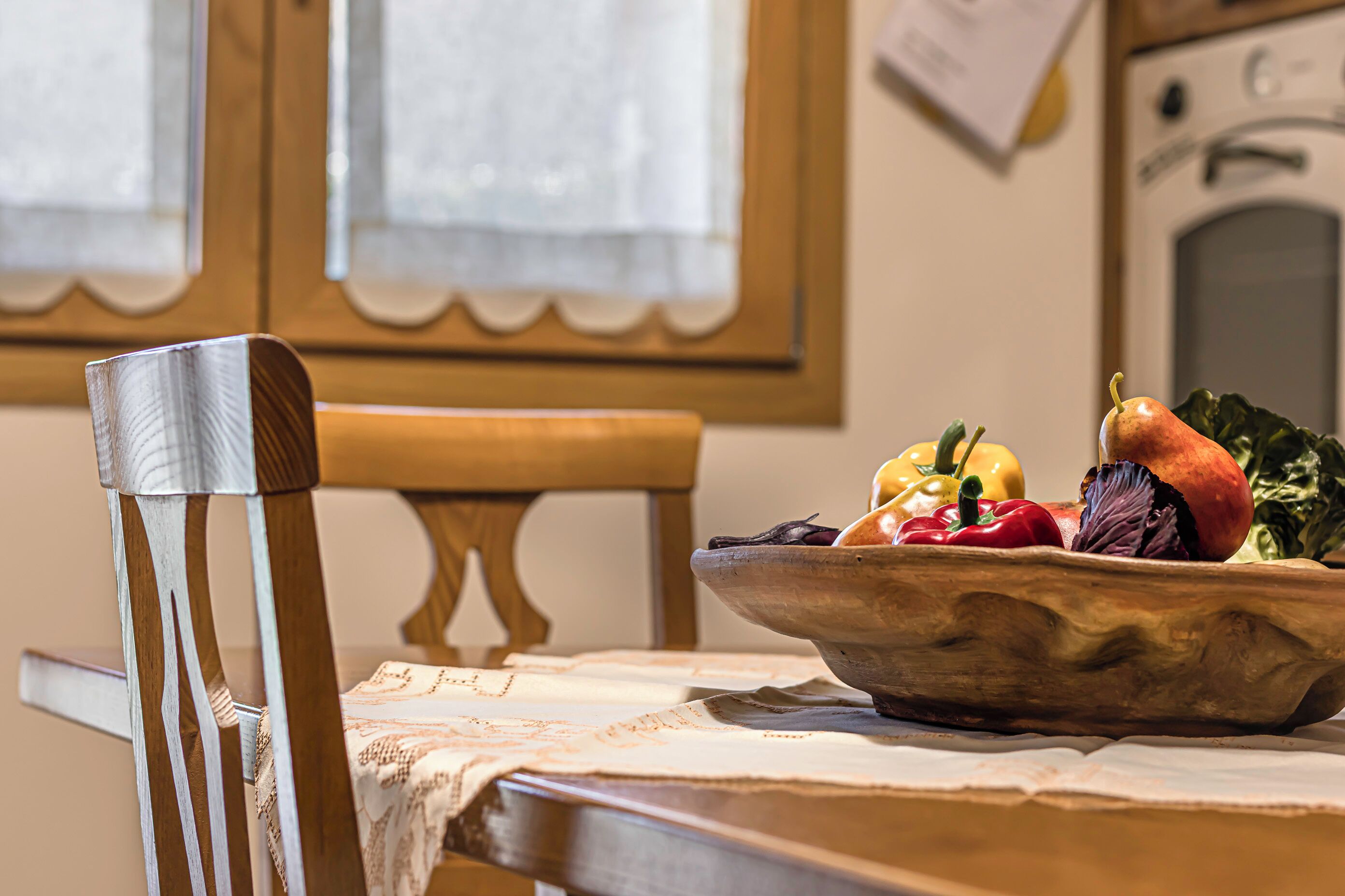 Een eettafel met een schaal fruit en groenten, een houten stoel en een raam met jaloezieën.