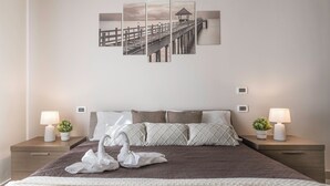 A neatly arranged hotel room with a large bed, two bedside tables with lamps, a wall-mounted artwork of a pier, and a decorative swan on the bed. - Apt Wanderlust 1 with swimming pool[Unesco-Prosecco] (Bagnolo)