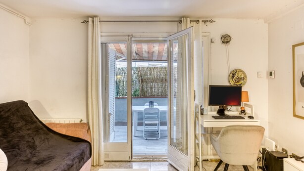 A room with a black sofa, a desk with a computer, and a sliding glass door leading to an outdoor area with a table and chair. - 'Irlulan' Apartment with Private Terrace and Wi-Fi (Platja d'Aro)
