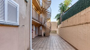 A narrow alleyway with a spiral staircase leading to a balcony, tiled floor, and a wall with a green hedge. - 'Irlulan' Apartment with Private Terrace and Wi-Fi (Platja d'Aro)