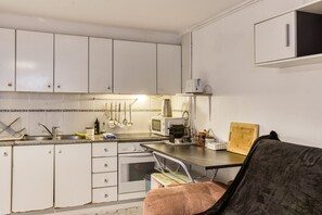 A compact kitchen with white cabinets, a microwave, a toaster, and a small dining area with a chair. - Apartment 'Irlulan' with Private Terrace and Wi-Fi (Platja d'Aro)