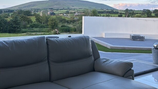Ein modernes Wohnzimmer mit einer weißen Ledersofa, einem großen Fenster mit Blick auf eine grüne Landschaft und Hügel.