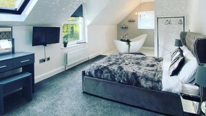 Ein modernes Schlafzimmer mit Dachfenster, einem großen Bett, einem Schreibtisch und einem Badezimmer im Hintergrund.