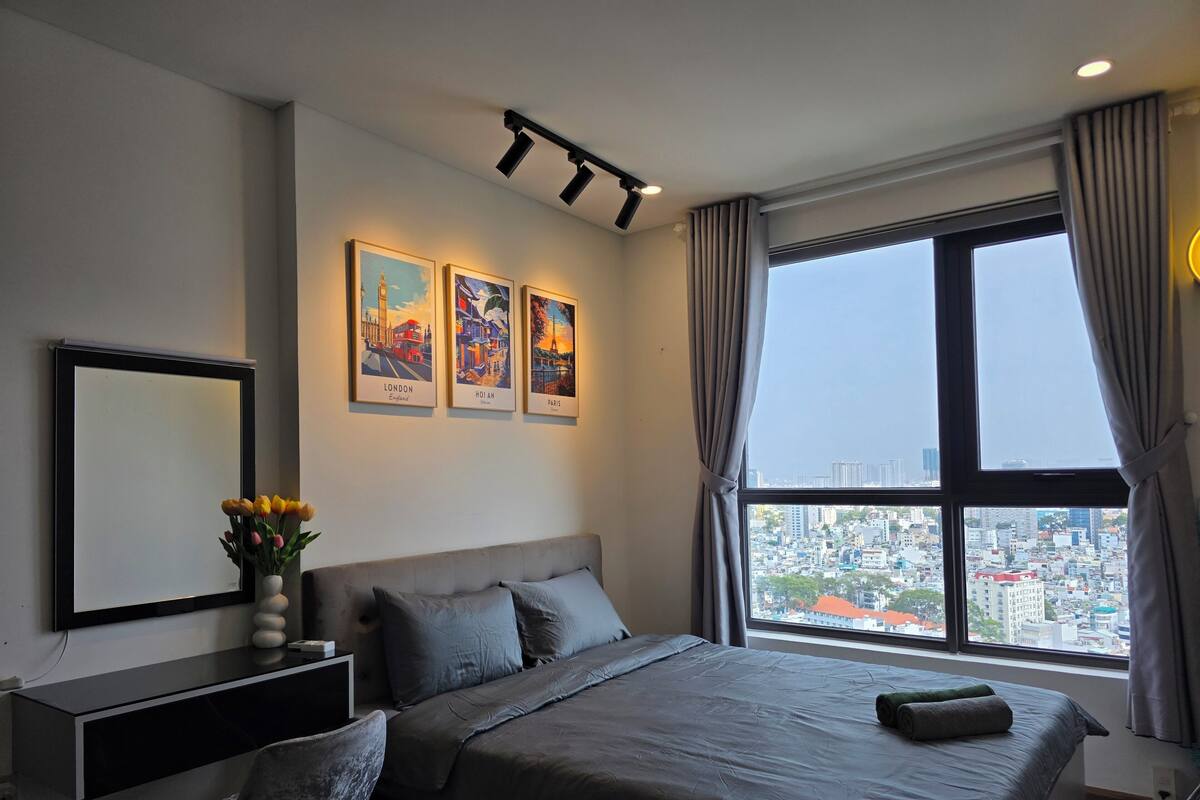 Une chambre moderne avec un grand lit, une table de chevet, un miroir et une vue sur la ville par une grande fenêtre.