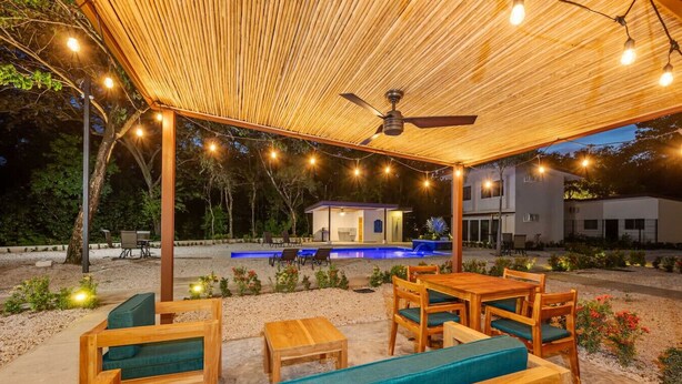 An outdoor patio with wooden furniture, a ceiling fan, and string lights.