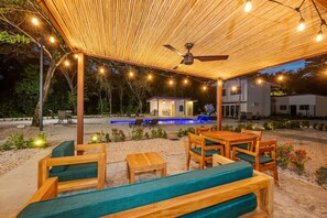 Eine Terrasse im Freien mit Holzmöbeln, einem Deckenventilator und Lichterketten.