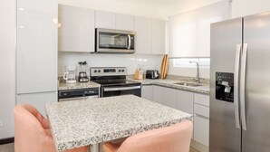 A modern kitchen with white cabinets, a stainless steel refrigerator, a microwave, a coffee maker, and a toaster.