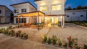 A modern two-story house with a covered patio area featuring outdoor furniture and string lights.