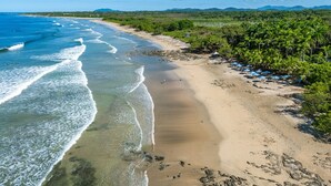 A beach with clear blue waters, sandy shore, and dense greenery. - Pool, Beach, AC, Fast WiFi | Avellanas Modern Home (Playa Avellanas)