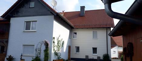 A two-story residential building with a satellite dish, a chimney, and a paved driveway.