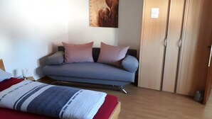 Une pièce comprenant un canapé, un lit, une armoire en bois et un tableau accroché au mur.