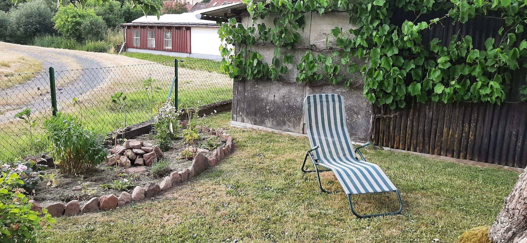 Un jardin avec une pelouse, une bordure en pierre et un fauteuil de jardin à rayures.