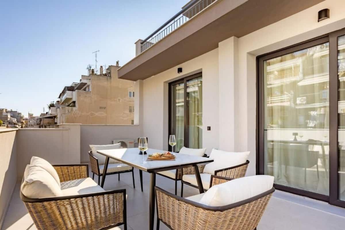 Eine Dachterrasse mit Esstisch, Korbstühlen, großen Schiebeglastüren und Blick auf die Stadt.