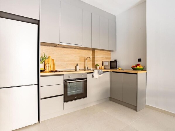 A modern kitchen with grey cabinets, a wooden countertop, a built-in oven, and a microwave.