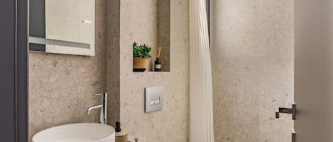 Un baño moderno con un lavamanos redondo, un inodoro y una ducha con cortina.