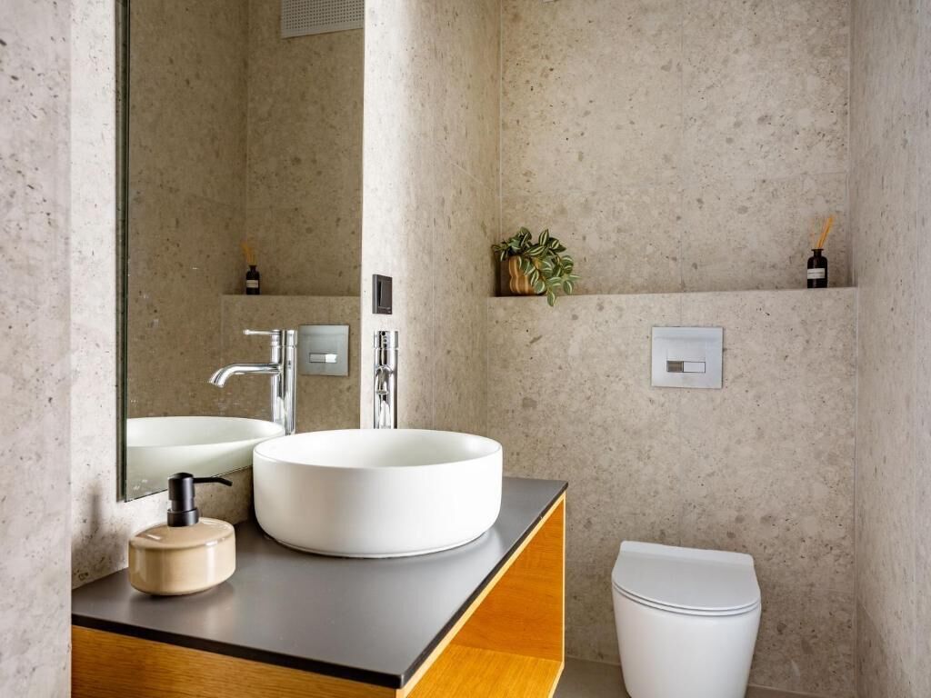 A modern bathroom with a large mirror, a round sink, and a toilet.