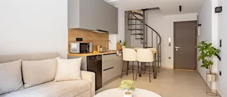Un salon moderne comprenant un canapé, une table basse ronde avec une plante, un coin cuisine avec un four à micro-ondes et un escalier en colimaçon menant à une autre pièce.