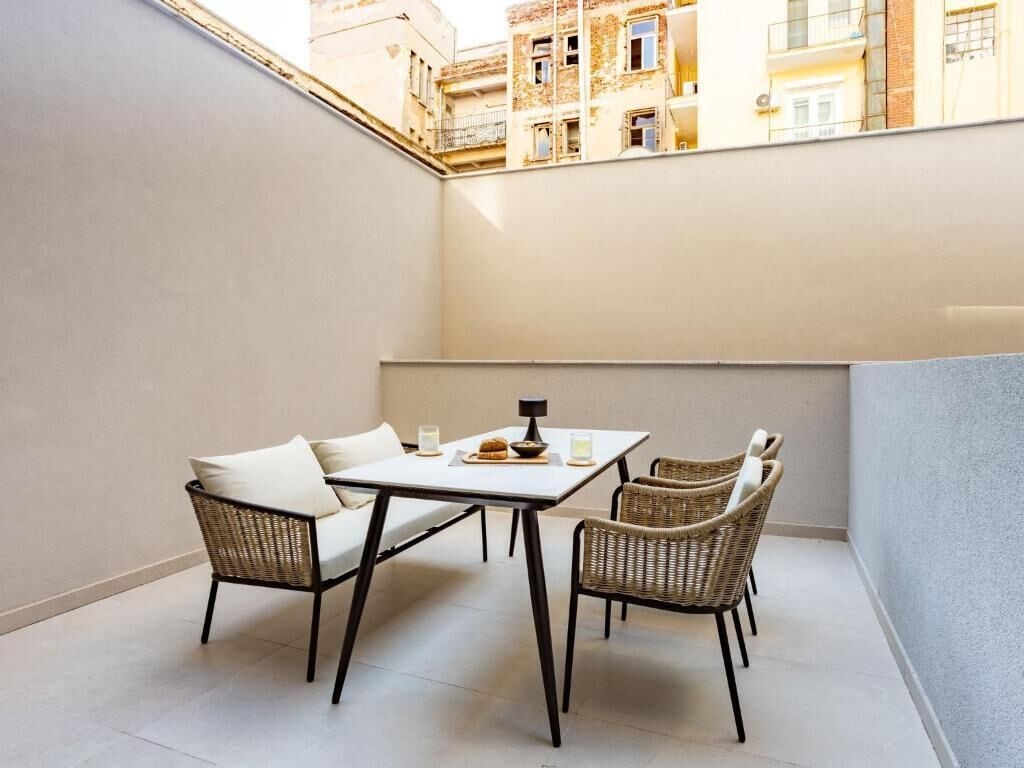A small balcony with a table and chairs, a view of buildings in the background.