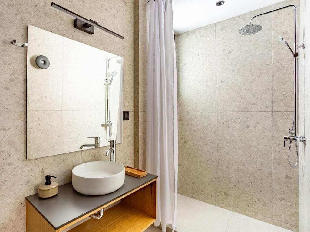 Un baño moderno con un lavabo redondo, un espejo, una ducha con cabezal de ducha manual y una cortina.