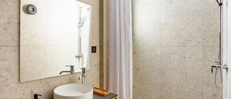 Un baño moderno con un lavabo redondo, un espejo, una ducha con cabezal de ducha manual y una cortina.