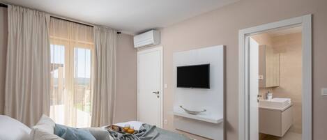 A modern hotel room with a bed, a TV mounted on the wall, a bathroom with a mirror and sink, and a balcony with curtains.