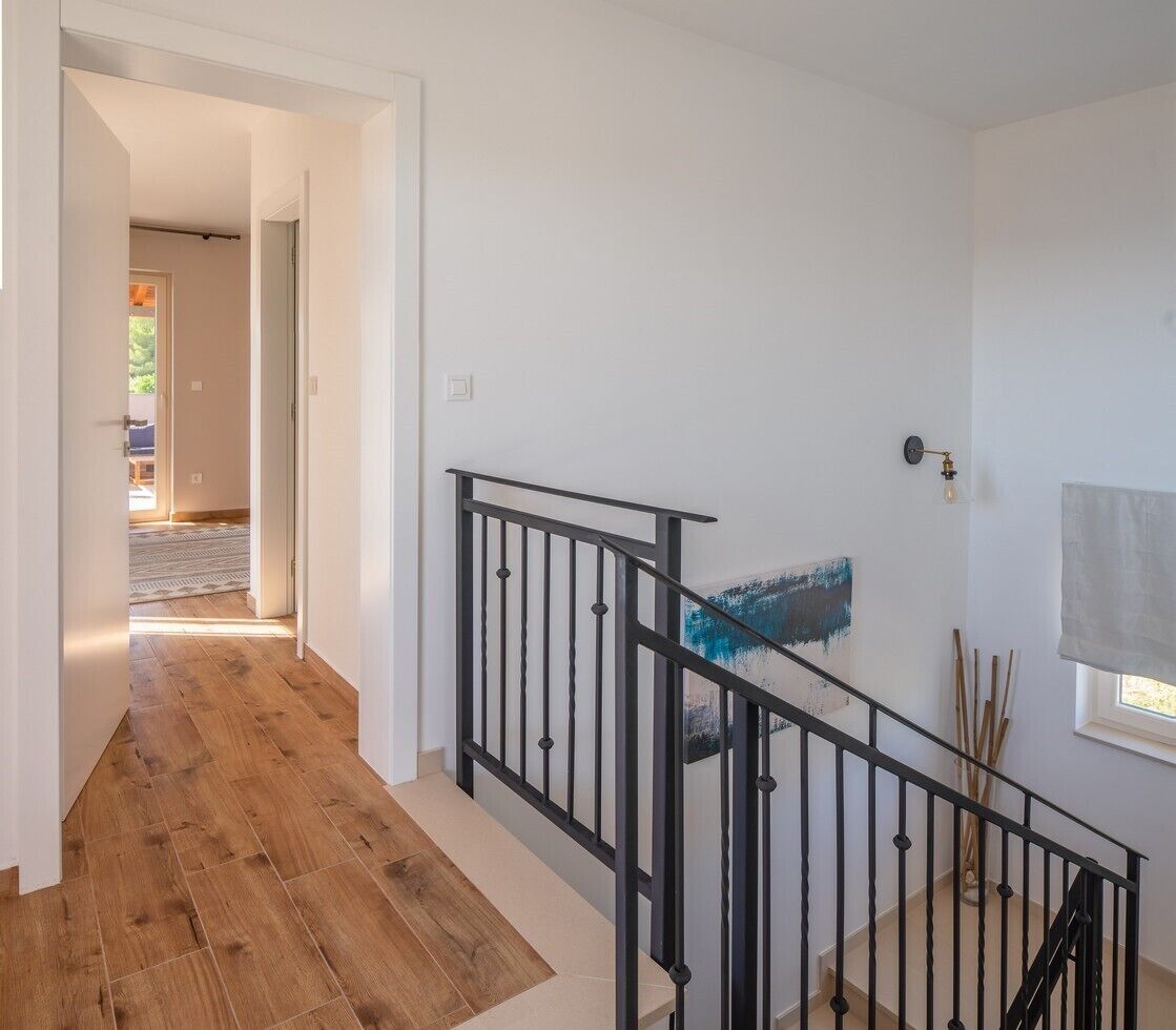 Ein Korridor mit Holzboden, der zu einer Treppe mit schwarzen Geländern führt.