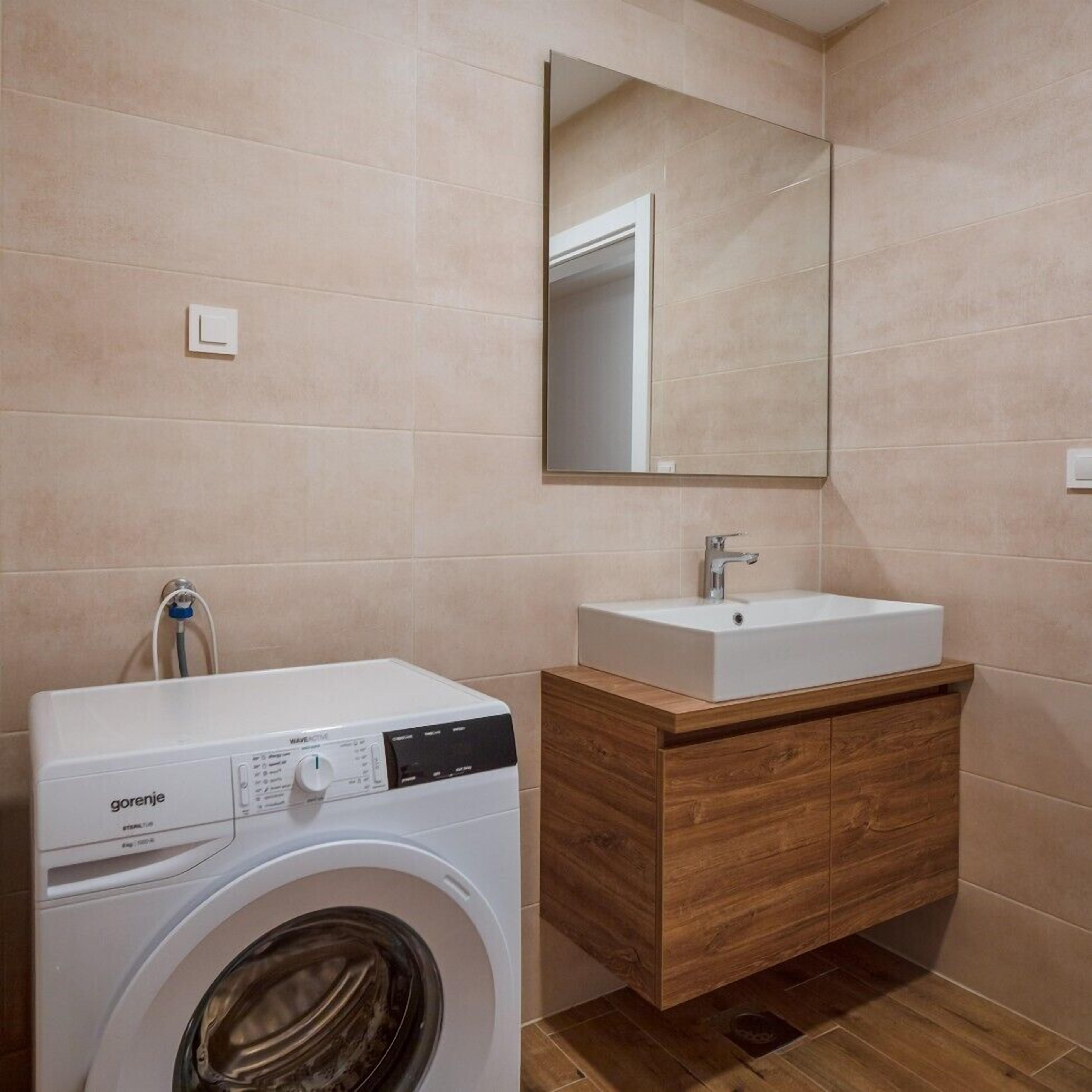 A modern bathroom with a washing machine, a wooden vanity with a sink, and a large mirror on the wall.