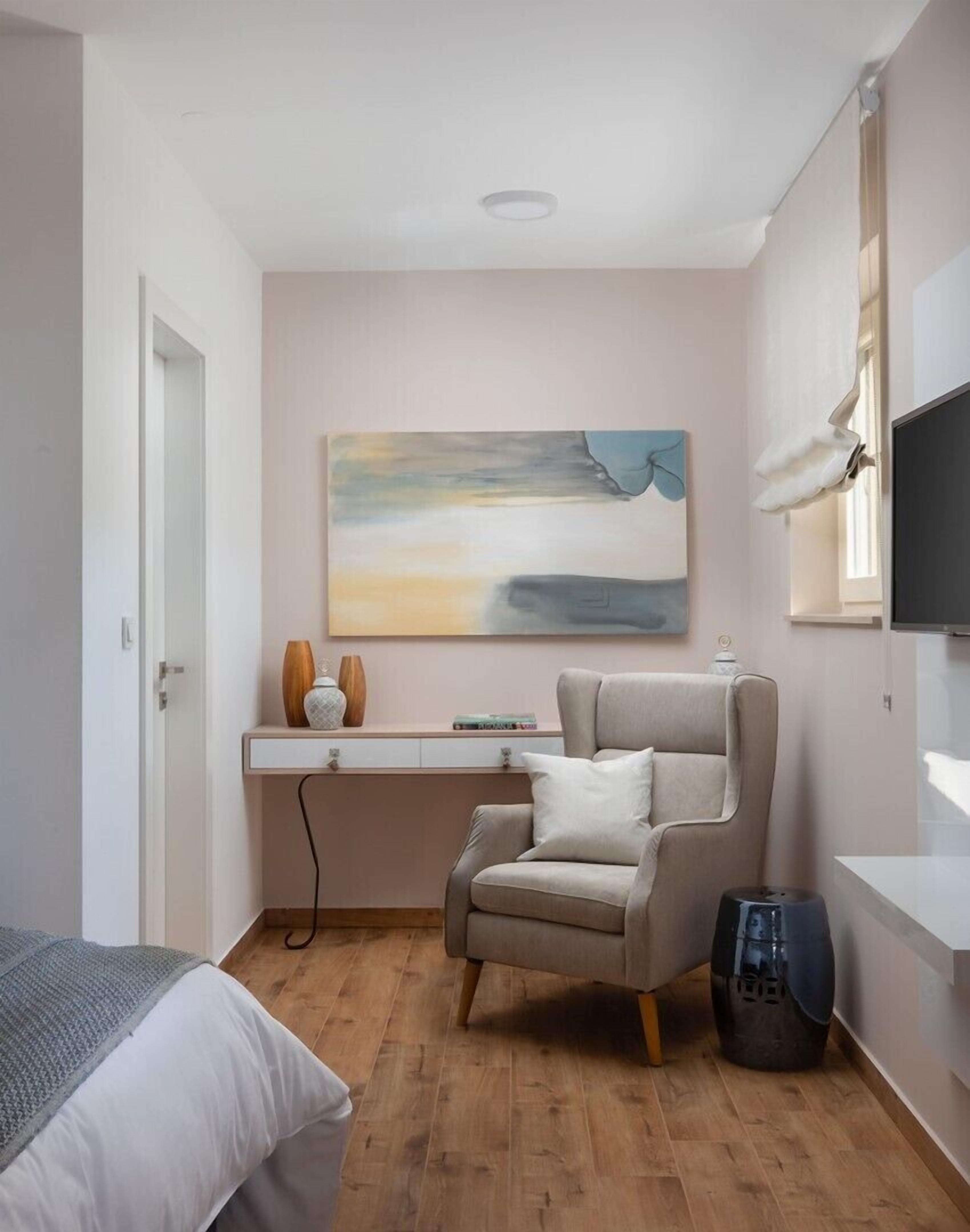 A modern bedroom with a bed, a desk, a chair, and a painting on the wall.