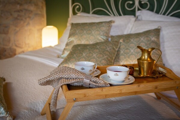 Un plateau en bois avec deux tasses et une théière, posé sur un lit agrémenté d’oreillers à motifs et d’une tête de lit.