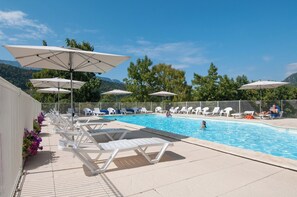 A pool area with sun loungers and umbrellas, surrounded by greenery and hills.