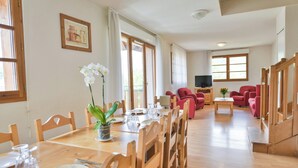 A dining area with a wooden table set for four, surrounded by wooden chairs. There is a potted orchid on the table.