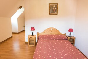 A bedroom with a wooden bed, two bedside tables with lamps, a slanted ceiling, and a framed picture on the wall.