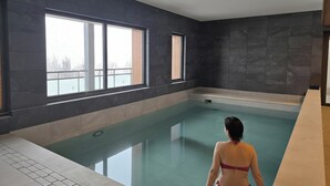 An indoor swimming pool with dark stone walls and large windows.