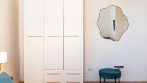 A room with a white wardrobe, a round mirror, a small round table, and a teal chair. - Rental in Rome Constance Apartment (Rome)
