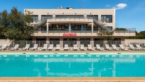 Un bâtiment moderne doté d’une piscine, de chaises longues et d’une enseigne indiquant la présence d’un restaurant et d’une pizzeria.