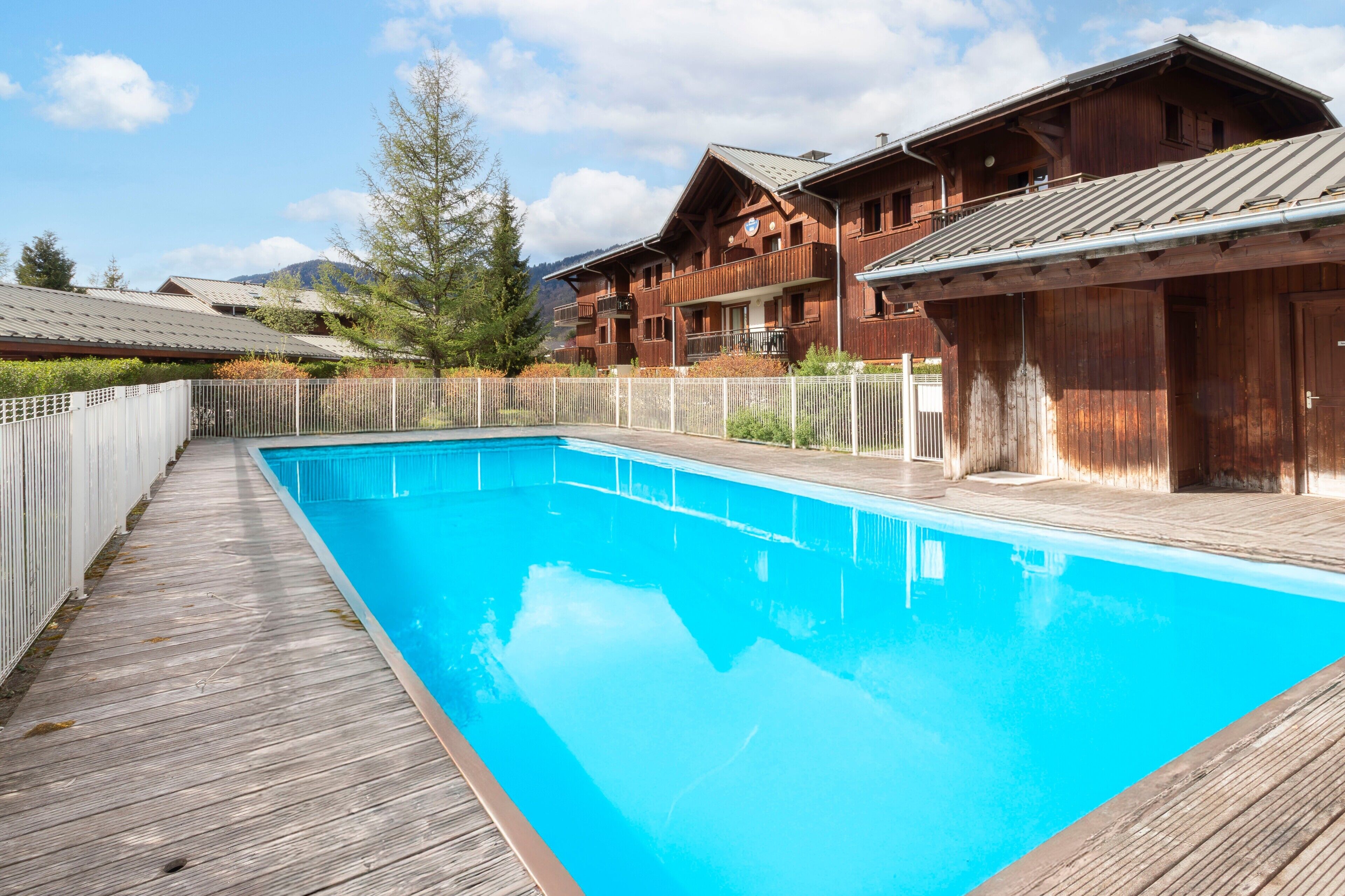 A wooden deck leading to a clear blue pool, surrounded by wooden buildings with balconies.